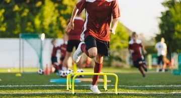 Sporty kids exercising and jumping over hurdles on the training field.